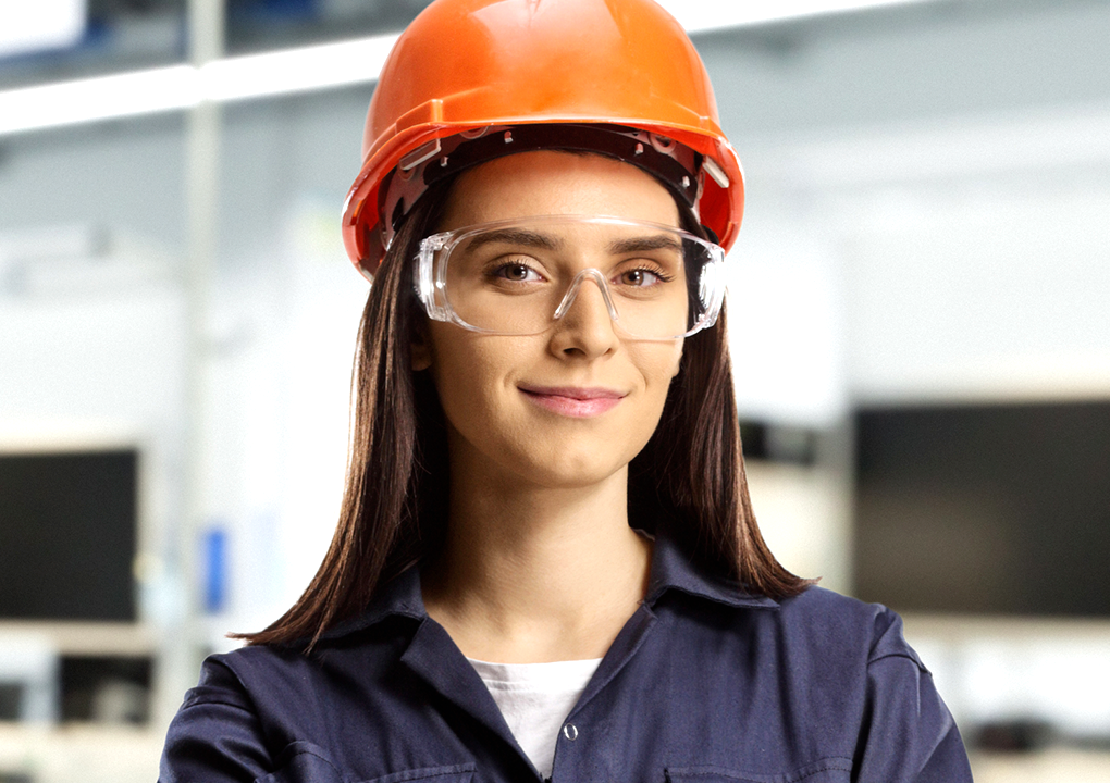 Mulher utilizando uniforme certificado NR-06, NR-10 e NR-38, com faixas refletivas e tecido de proteção, em ambiente industrial seguro.